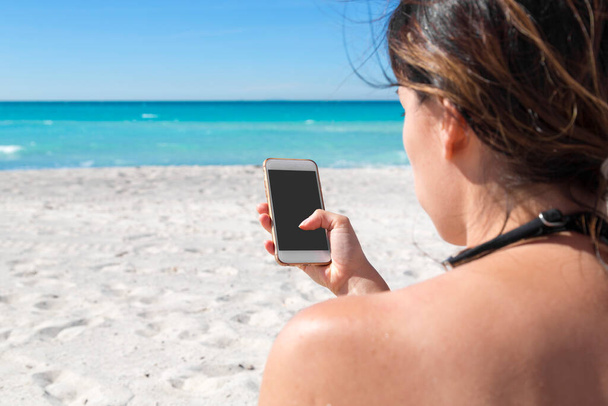 Beach holiday woman holding smart phone, texting and tapping. Summer vacation with the blue sea in the background - Foto, Bild