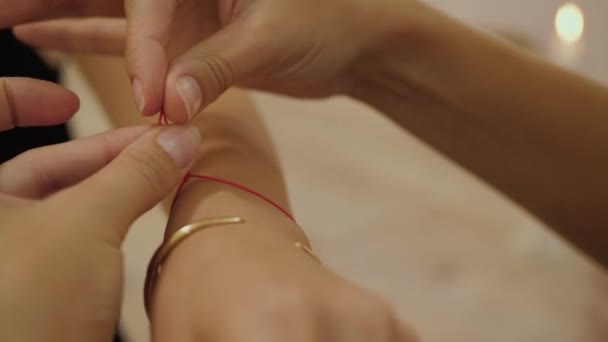 Religieus ritueel van dichtbij. Vrouwelijke handen binden een rode draad om de pols van de vrouw als zegen voor geluk en vrede. - Video