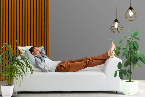 Hymyilevä mies makaa ja rentouttava sohvalla kotona olohuoneessa
 - Valokuva, kuva