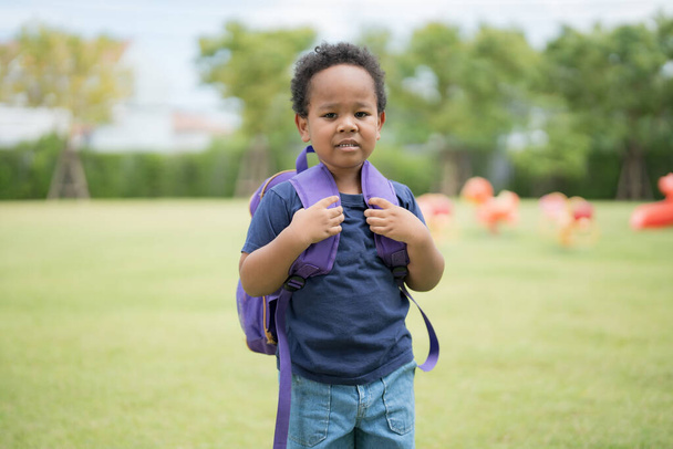 Słodki chłopczyk niosący torbę szkolną z uśmiechniętą twarzą czekający na powrót do domu.. - Zdjęcie, obraz
