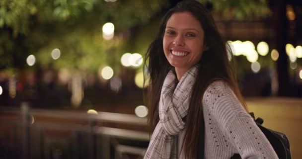 Красивая белая девушка в полосатом шарфе смотрит в глаза ночью на городской улице. Тысячелетняя женщина с рюкзаком улыбается в камеру. 4k - Кадры, видео