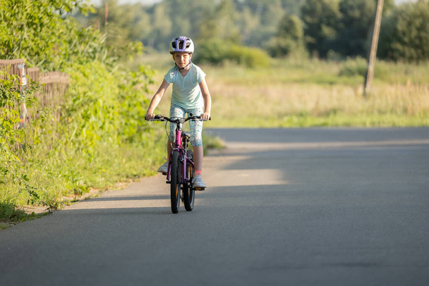 Enfant d'âge scolaire sur un vélo, fille motard chevauchant une rue vide dans une zone rurale, une personne, vue de face, espace de copie. Un motard, un petit cycliste seul. Sports, loisirs, activités récréatives - Photo, image