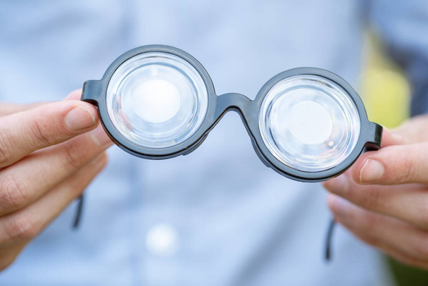 Hombre sosteniendo grandes gafas de juguete con grandes lentes gruesas, gafas simples en las manos detalle del objeto, primer plano, una persona. Visión, cuidado de la vista y salud concepto abstracto, símbolo, gafas graduadas - Foto, imagen