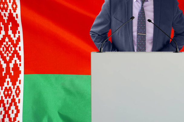 Tribune s mikrofonem a muž v obleku na pozadí běloruské vlajky. Podnikatel a tribun na pozadí běloruské vlajky. Politik na pódiu s mikrofony pozadí Běloruská vlajka. Konference - Fotografie, Obrázek