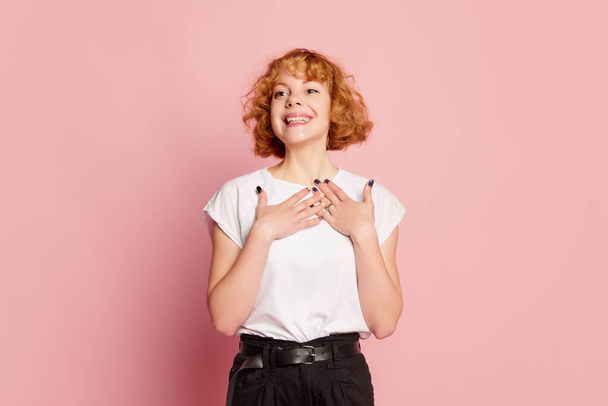 Happy smile. Emotional young girl with curly hair wearing white t-shirt isolated on pink studio background. Human emotions, facial expression, beauty concept. Copy space for ad. - Fotó, kép