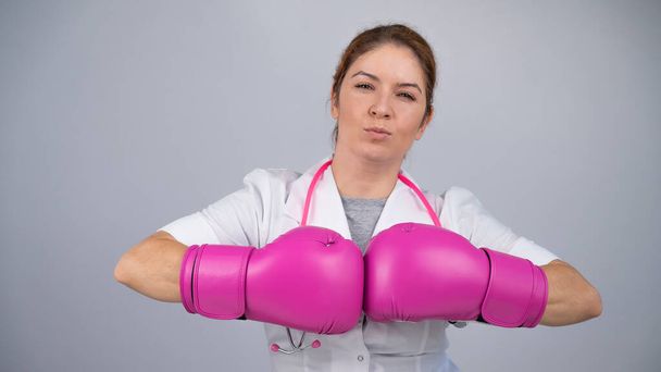 Kobieta w różowych rękawiczkach bokserskich z różową wstążką na szarym tle. Walka z rakiem piersi - Zdjęcie, obraz
