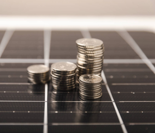 Panel słoneczny i monety. Koncepcja oszczędzania pieniędzy i czystej energii.Korzyści ekonomiczne energii odnawialnej. - Zdjęcie, obraz