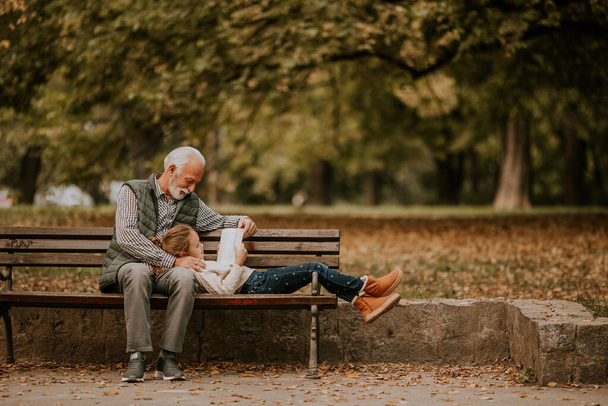 Komea isoisä viettää aikaa lapsenlapsensa kanssa penkillä puistossa syyspäivänä - Valokuva, kuva