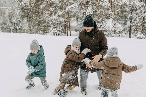 Father playing with children on snowy winter day. Kids trying to push dad on snow. - Photo, Image