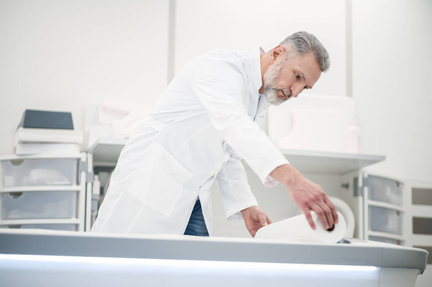 RM. Médico de cabelos grisalhos masculino em um casaco de laboratório trabalhando no centro de diagnóstico - Foto, Imagem