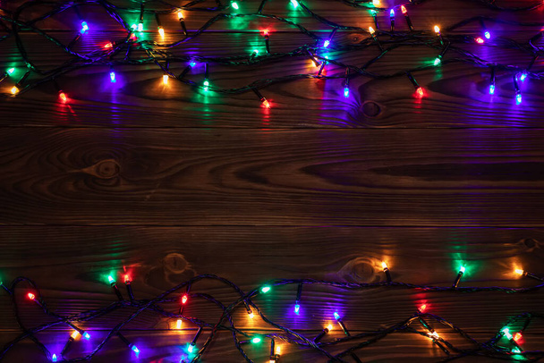 Christmas lights background, copy space. Holiday shiny garland border top view on brown wooden planks surface. Xmas tree decorations, winter holidays illumination - Foto, imagen