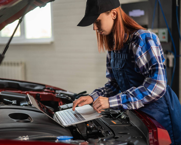 Woman auto mechanic doing engine diagnostics using laptop - Foto, Imagen