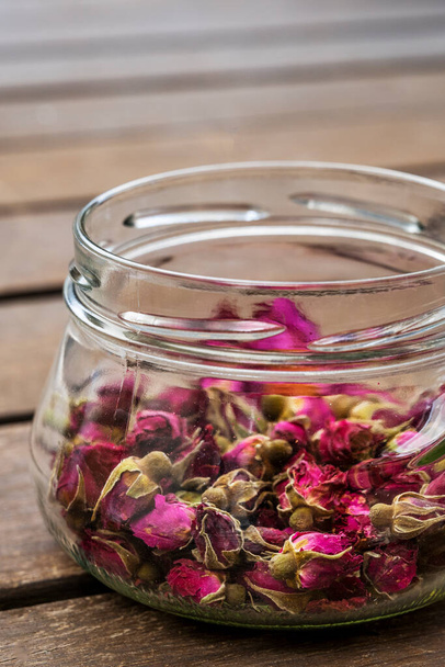 Beautiful glass jars with tea roses on acacia plank surface - Foto, imagen
