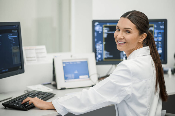 Hivatásos munkás. Sötét hajú női orvos ül a laptopnál és elemzi az MRI eredményeket. - Fotó, kép