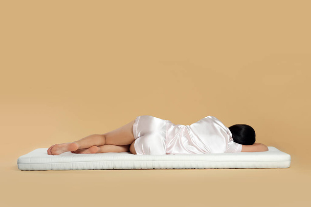 Young woman lying on soft mattress against beige background, back view - Fotografie, Obrázek