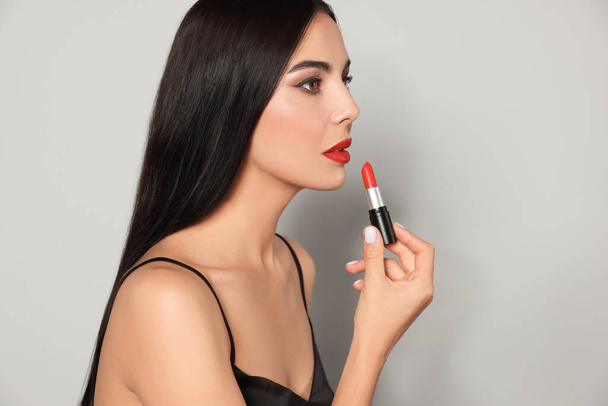 Young woman with beautiful makeup holding red lipstick on light gray background - Foto, afbeelding