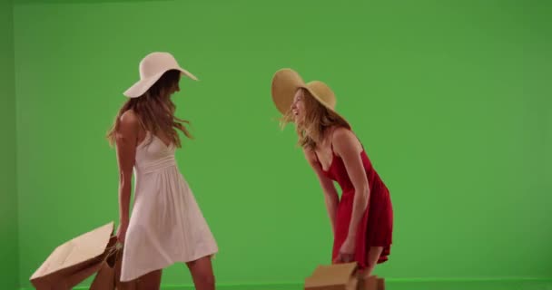 Twee jonge aantrekkelijke meisjes in jurken die boodschappentassen dragen en ronddraaien op een groenscherm. Een paar leuke witte meisjes draaien in de zomer jurken na het winkelen op groen scherm. 4k - Video