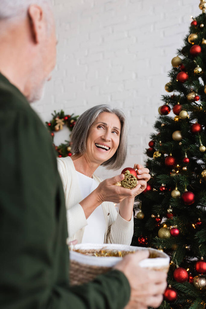 joyful middle aged woman with grey hair decorating christmas tree near husband  - Photo, Image