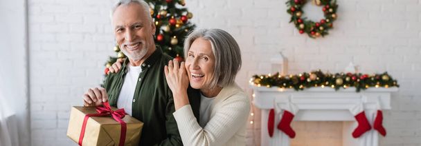 happy middle aged woman hugging bearded husband with christmas present, banner - Photo, Image