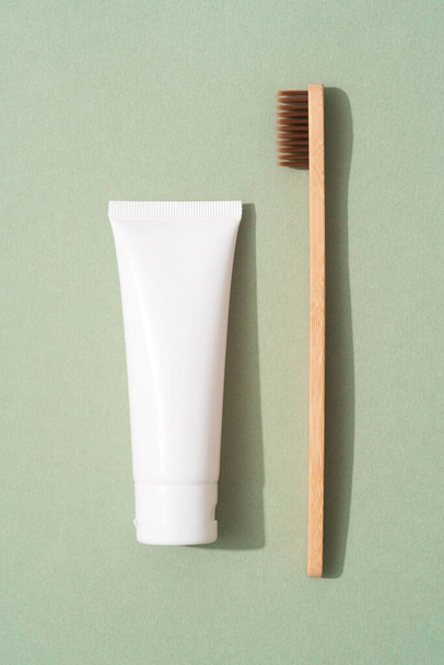 Vertical image of wooden bamboo toothbrush and tube with organic mineral toothpaste over green background. White plastic tube with toothpaste. Eco bath products, mockup - Фото, зображення