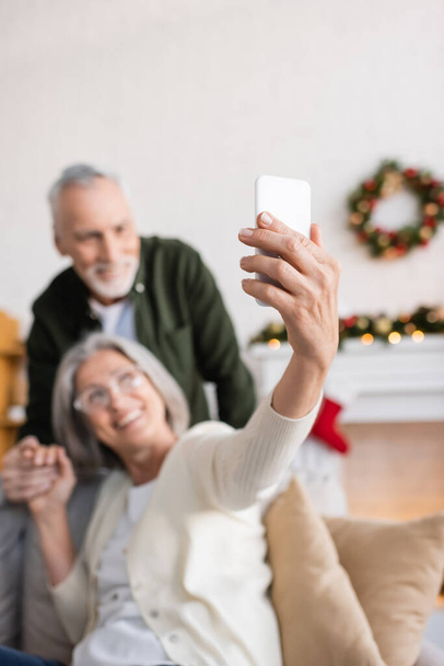 happy mature woman in glasses taking selfie with husband on blurred background  - Photo, Image