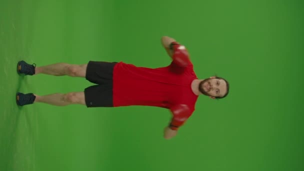 Vertical Video,Vertical View .Young Motivated Professional Bearded Fighter Making Winning Gesture with Hands Up in Fighting Gloves on a Green Screen, Chroma Key.Man Kickboxing and Sport Concept. - Footage, Video