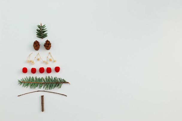 Christmas tree made with evergreen fir, pine cones, red berries and branches on white background. Minimal holiday flat lay composition. Winter creative concept. Copy space. - Photo, Image