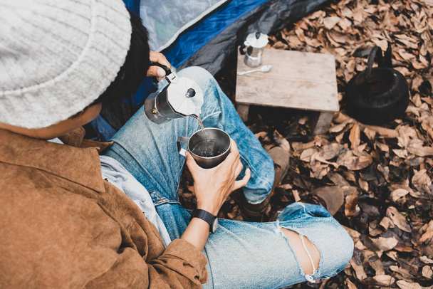 Ασιάτισσα λεσβία κάθεται ρίχνει ζεστό νερό του espresso με ιταλική Moka καφετιέρα πίνοντας σε ένα δάσος στις διακοπές, ταξιδιώτη υπαίθρια η σκηνή χαρούμενο ενιαίο κάμπινγκ πικνίκ το πρωί - Φωτογραφία, εικόνα