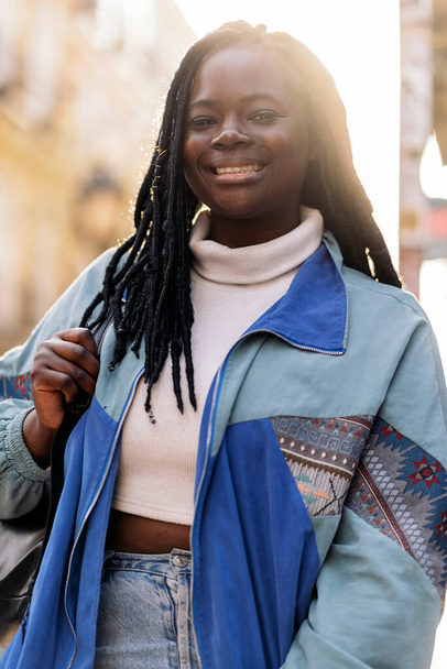Happy young african woman with cool braids smiling and looking at camera in the city. - Foto, Imagem