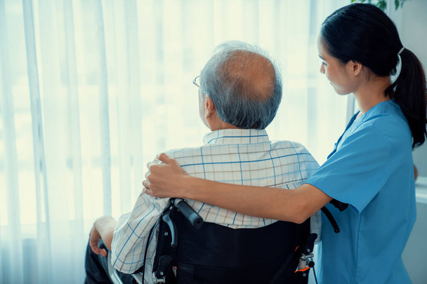 Rear view of a caregiver and her contented senior man gazing out through the window. Elderly health care, nursing homes for the elderly, and pensioner life - Photo, Image