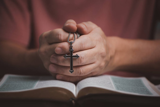 Open holy bible book with people hands folding and holding cross necklace in the middle book pray to God - Fotoğraf, Görsel