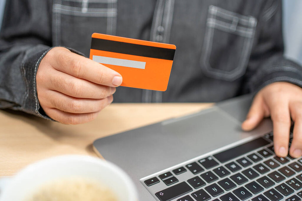 Ο άνθρωπος πληρώνει με πιστωτική κάρτα και φορητό υπολογιστή κάθεται στο γραφείο - Φωτογραφία, εικόνα