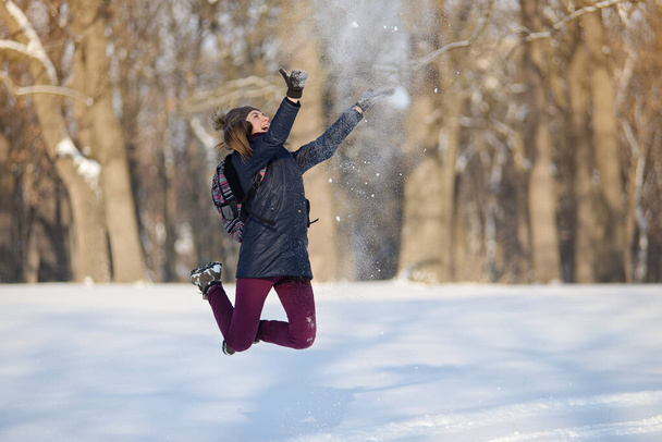 Onnellinen nuori nainen hyppii ja oksentaa lunta luminen talvipuisto. Aurinkoinen sää. Talvikausi. - Valokuva, kuva