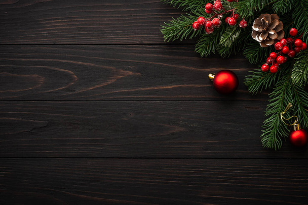 Kerstkaart. Fir boom brunch en rode decoraties op houten achtergrond. plat lag met kopieerruimte. - Foto, afbeelding