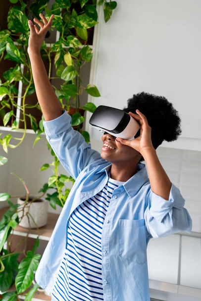Fille noire excitée portant des lunettes en utilisant VR AR à la maison, heureuse jeune femme africaine amoureuse de plantes portant des lunettes 3D profitant d'une visite de jardin en réalité virtuelle 360, testant la technologie future - Photo, image