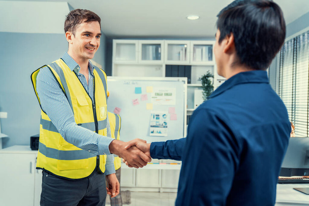 An engineer with a protective vest handshake with an investor in his office. Following a successful meeting, employee and employer form a partnership. - Foto, Imagen