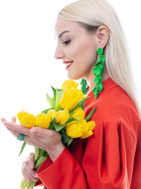 Egy divatos pillanatkép. Egy gyönyörű szőke pózol fényes ruhában, fehér háttérrel, sárga tulipánnal a kezében. Közelkép. - Fotó, kép