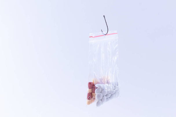 The Pharmaceutical Trap and Drug Addiction - Colored Pills or Tablets Hanging in Small Ziplock Bag on a Fishing Hook Against the White Background - Photo, Image