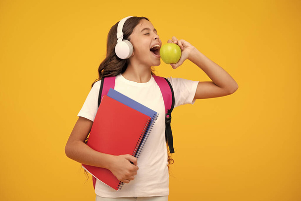 Amazed teen girl. Back to school. Full length of teenager school girl with backpack hold aplle ready to learn. School children with school bag on isolated yellow studio background - 写真・画像