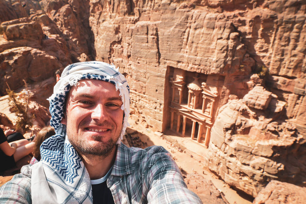 Kaukázusi férfi turista állni nézőpont Petra ókori város felett kincstár vagy Al-khazneh hogy okostelefon fotó mosoly. Jordan, a hét csoda egyike. UNESCO Világörökség része. - Fotó, kép