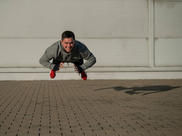 A man in a hoodie jumps while doing push-ups outdoors - Foto, Imagen