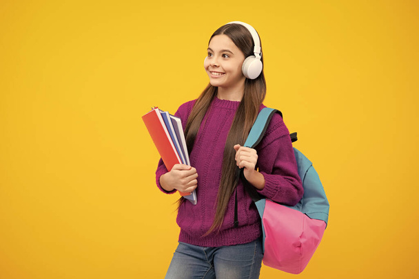 Schoolgirl, teenage student girl in headphones hold books on yellow isolated studio background. School and music education concept. Back to school - Foto, afbeelding