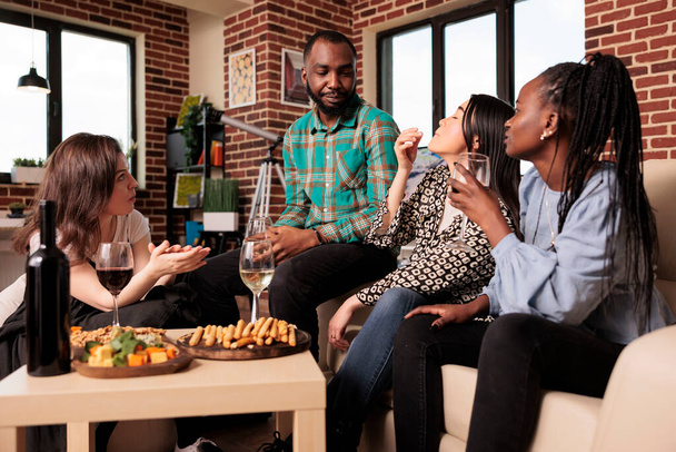 Afrykański amerykański młody człowiek dorosły poważnie mówi, dyskutuje, rozmawia, rozmawia z kulturowo zróżnicowaną grupą dorosłych ludzi na zjeździe domowym w salonie. Wielokulturowi przyjaciele pijący wino. - Zdjęcie, obraz