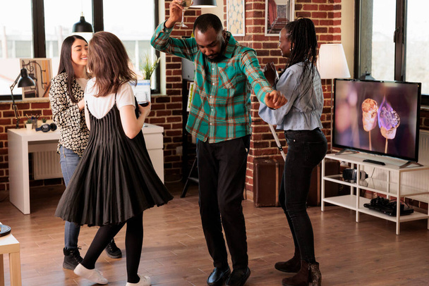 Jovem adulto afro-americano do sexo masculino se divertindo, arrepiando, dançando, sorrindo, rindo, desfrutando da vida social acompanhada por mulheres na festa do apartamento. Pessoas multiculturais por aí. - Foto, Imagem