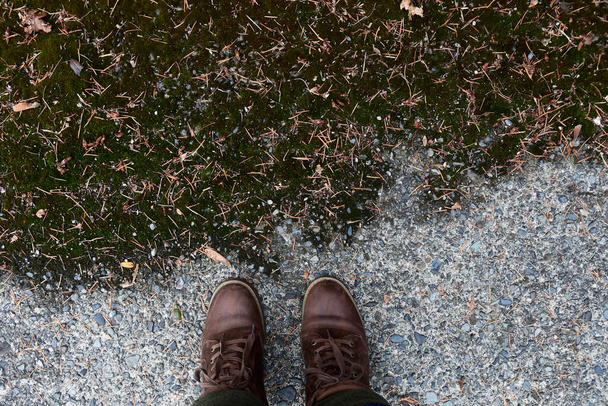 Une image d'une paire de bottes de randonnée marron usé et un chemin couvert de mousse verte épaisse. - Photo, image