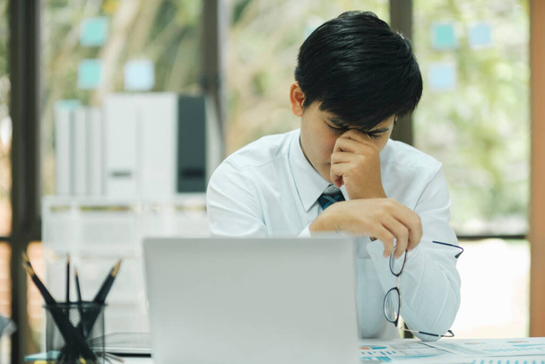 Young professional and focused businessman with eyeglasses stressed using laptop to work, analyzing data, and planning business strategies to improve sale profit while sitting at desk in the office. - Foto, Imagem