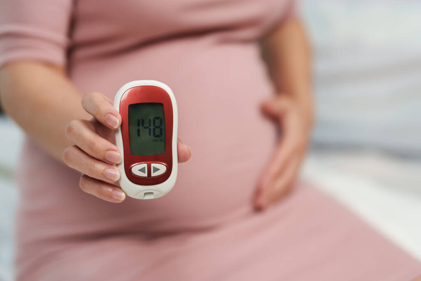 close up of pregnant woman holding glucose meter with result of measurement sugar high level. gestational diabetes concept. - Valokuva, kuva