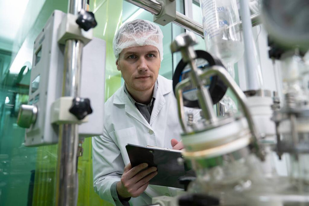 Porträt eines Wissenschaftlers, der mit wissenschaftlichen Geräten in einem Labor Cannabisöl extrahiert. Konzept der Cannabis-Extraktion für alternative medizinische Behandlungen - Foto, Bild