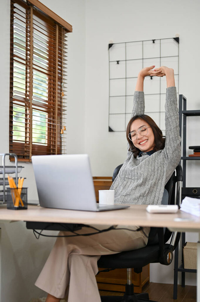 Retrato, escalofriante y feliz joven empresaria asiática o trabajadora de oficina estirando los brazos en su escritorio, relajándose después del trabajo. - Foto, Imagen