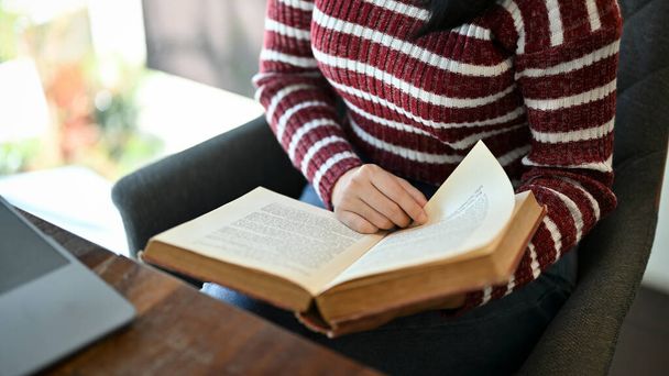 Una joven estudiante universitaria asiática inteligente leyendo un libro, investigando información sobre el libro de texto mientras está sentada en la biblioteca del campus. imagen recortada - Foto, imagen
